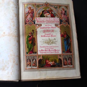 May include: A vintage religious book cover with a colorful illustration of Jesus Christ and Mary. The cover features a gold frame with ornate details and a title that reads "Das Leben unseres Herren u. Heilandes Jesus Christus und seiner jungfräulichen Mutter Maria." The book was published by C.G. Businary Regens in Einsiedeln, New York, Cincinnati, and printed by Carl A. Michaelis Deuriger.