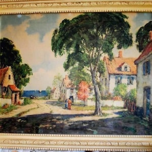May include: A framed landscape painting depicting a quaint village scene. The artwork features a road lined with houses, trees, and figures. The painting is in a cream-colored ornate frame, adding to its vintage aesthetic.