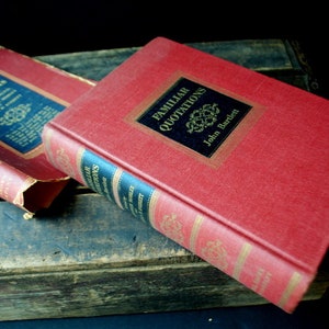 May include: Two red hardcover books titled "Bartlett's Familiar Quotations" and "Familiar Quotations" by John Bartlett. The books are on a wooden surface.