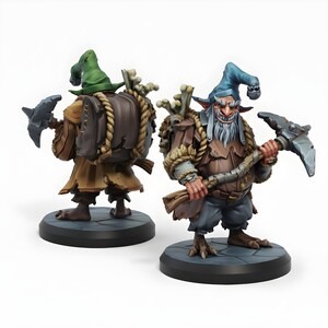 Op de afbeelding: Twee miniatuur fantasyfiguren van gnome-achtige karakters. Eén figuur is van achteren te zien, met een groene hoed en een rugzak. De andere figuur staat naar voren, met een pikhouweel en een blauwe hoed. Beide figuren hebben gedetailleerde kleding.