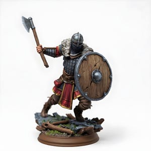 May include: A detailed figurine of a Viking warrior in battle stance. The figure wears a helmet, chainmail, and a red and gold tunic. He holds an axe and a round wooden shield. The base features rocks and logs.