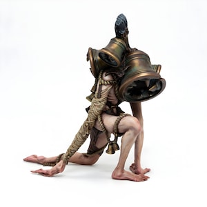 May include: A detailed figurine of a humanoid creature kneeling on a white surface. The figure has a pale complexion, wrapped in rope and carrying large bronze bells on its back. Small bells hang from the rope. The figure has a dark, textured headpiece.