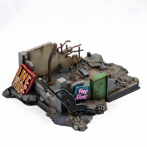 May include: A miniature diorama depicting a post-apocalyptic scene with a partially destroyed building. Features neon signs that read "LIVE NUDE" and "Peep Show". The scene includes rubble, a green door, and a bent metal pipe.