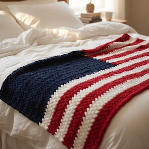Op de afbeelding: Een handgemaakte deken met een patriottisch ontwerp. De deken heeft een marineblauw gedeelte en afwisselend rode en witte strepen, die doen denken aan een vlag. De deken is gedrapeerd over een bed met wit beddengoed, wat een warme en uitnodigende uitstraling creëert.