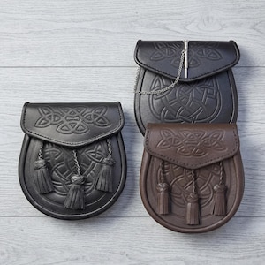 Peut inclure: Trois sporrans en cuir noir et marron, chacun avec un motif de nœud celtique en relief sur le rabat. Le sporran noir a trois glands, tandis que le marron en a trois. Le sporran noir supérieur a une chaîne et une épingle en métal.