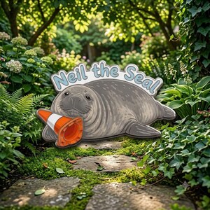 Peut inclure: Une plaque de jardin plate représentant un phoque gris au repos avec un cône de signalisation orange et blanc. Le texte "Neil the Seal" est écrit en lettres bleu clair avec un contour blanc au-dessus du phoque sur le panneau.