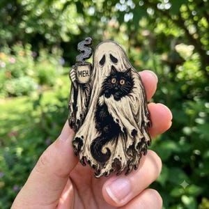 May include: A metal enamel pin featuring a cream-colored ghost draped in a sheet, holding a mug with the text MEH. A black cat with wide yellow eyes is nestled within the folds of the ghost's sheet, with steam rising from the mug above the ghost.