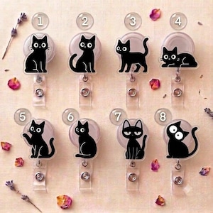 Könnte beinhalten: Acht einziehbare Ausweishalter mit schwarzen Katzensilhouetten und weißen Augen, nummeriert von eins bis acht. Jeder runde Halter verfügt über ein transparentes Kunststoffband und einen Metalldruckknopf und zeigt eine individuelle Katzenpose.