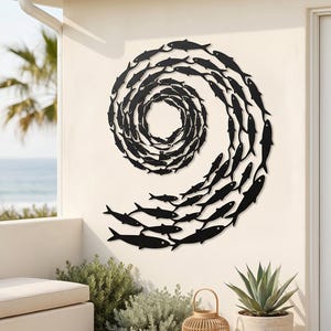 Peut inclure: Décoration murale en métal noir représentant un banc de poissons en spirale. Les poissons créent un motif tourbillonnant, adapté à la décoration intérieure ou extérieure. L'œuvre est fixée sur un mur crème.