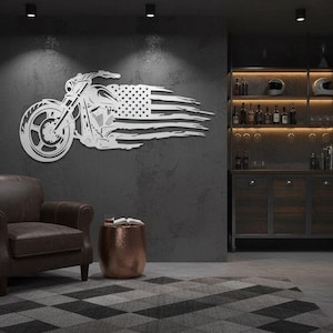 May include: A metal wall art piece depicting a motorcycle with an American flag design. The artwork is mounted on a dark gray wall in a room with a leather armchair, a copper side table, and a bar area with liquor bottles.