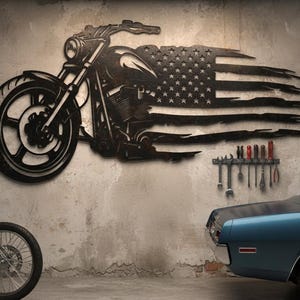 May include: Black metal motorcycle wall art with an American flag design. The motorcycle is depicted in profile, with the flag incorporated into the design. A classic blue car and a motorcycle are in the foreground.