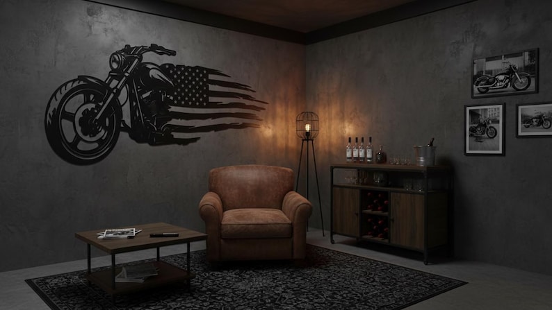 May include: A black metal motorcycle wall art piece with an American flag design. The artwork is mounted on a gray wall in a room with a leather armchair, a wooden cabinet, and framed motorcycle prints.