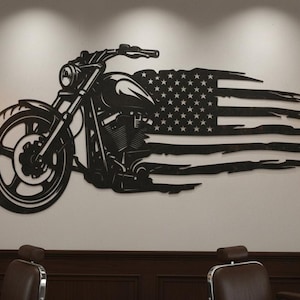 May include: Black metal wall art featuring a motorcycle design integrated with a distressed American flag. The motorcycle is detailed with visible engine components and a large front wheel. The artwork is mounted on a neutral-colored wall.