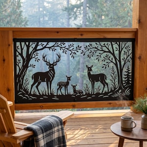 Op de afbeelding: Zwart metalen decoratief paneel met een silhouet van een hertenfamilie tegen een bosachtergrond. Het paneel is omlijst door houten balken en maakt deel uit van een terrasleuning. De scène omvat een bok, twee hinden en twee kalveren.
