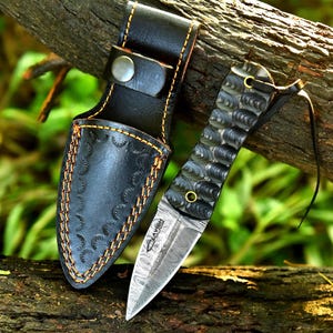 May include: A white ceramic mug with a black handle and the text "But First, Coffee" in a bold, black font. The mug is set against a blurred background, highlighting its clean design.