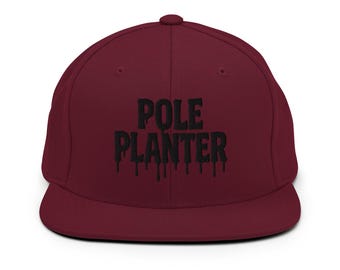 May include: A burgundy baseball cap with a flat peak. The cap displays the text "POLE PLANTER" in black, with a dripping effect. The cap has a structured fit and a button on top.