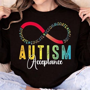 Puede incluir: Camiseta negra de manga larga con las palabras "AUTISM Acceptance" en un diseño colorido. El diseño incluye un símbolo de infinito con las palabras "Advocate, Educate, Accommodate, Include". La camiseta es de material suave.
