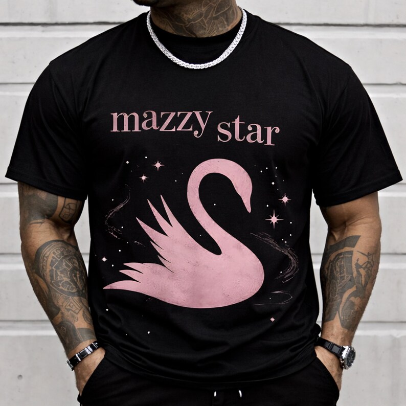 May include: Black t-shirt featuring the text "mazzy star" in pink above a pink swan graphic. The swan is set against a starry background. The shirt is a classic crew neck style.