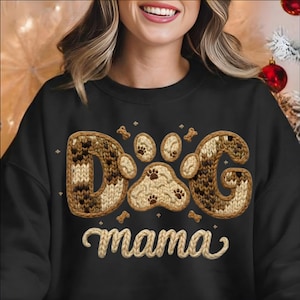 Peut inclure: Sweat-shirt noir avec l'inscription "Dog mama" dans un motif tricoté. Le mot "Dog" est épelé avec un motif tricoté marron et crème, et un motif de pattes. De petits os et des empreintes de pattes sont dispersés autour du motif.