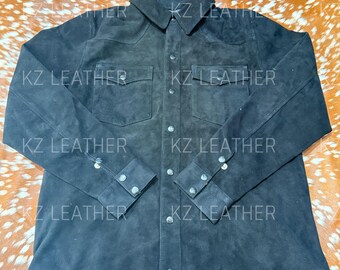 Peut inclure: Une chemise en daim noir avec une fermeture boutonnée, deux poches de poitrine et des manches longues. La chemise a un col classique et des poignets boutonnés. Le texte "KZ LEATHER" est visible.