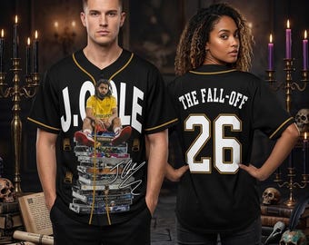Pode incluir: Uma camisa de beisebol preta com detalhes dourados, apresentando um gráfico de J. Cole sentado em uma pilha de fitas cassete na frente. A parte de trás exibe o texto THE FALL-OFF e o número 26 em branco com contornos dourados.