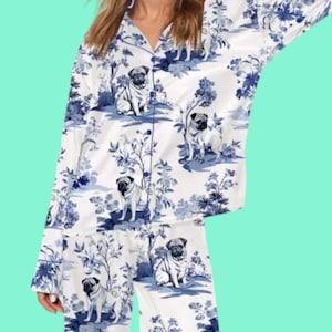 May include: White pajama set with a blue toile pattern featuring pugs and floral elements. The long-sleeved top has a button-down front and the pants have an elastic waistband. The fabric has a silky sheen.