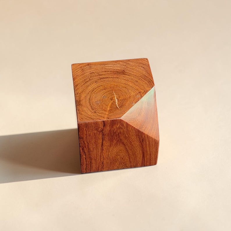 May include: A geometric wooden sculpture with a rich, reddish-brown hue. The block-shaped piece features a diagonal cut on one side, revealing a lighter wood grain. The sculpture is a unique decorative item.