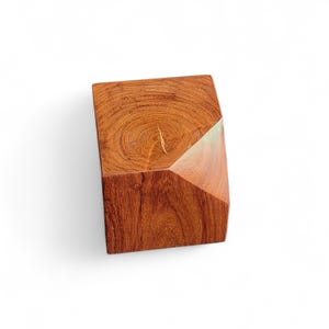 May include: A geometric wooden block with a natural wood grain pattern. The block is a reddish-brown color and has a faceted design on one side. The wood grain is visible on the top surface.