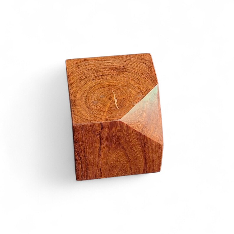 May include: A geometric wooden block with a natural wood grain pattern. The block is a reddish-brown color and has a faceted design on one side. The wood grain is visible on the top surface.