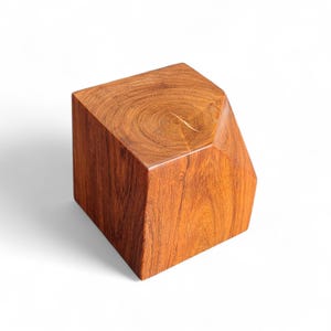 May include: A solid, geometric wooden block with a rich, reddish-brown hue. The block has a unique, asymmetrical shape with a flat top and a polished finish, showcasing the natural wood grain. The dimensions are approximately 10 inches wide, 10 inches deep, and 8 inches tall.