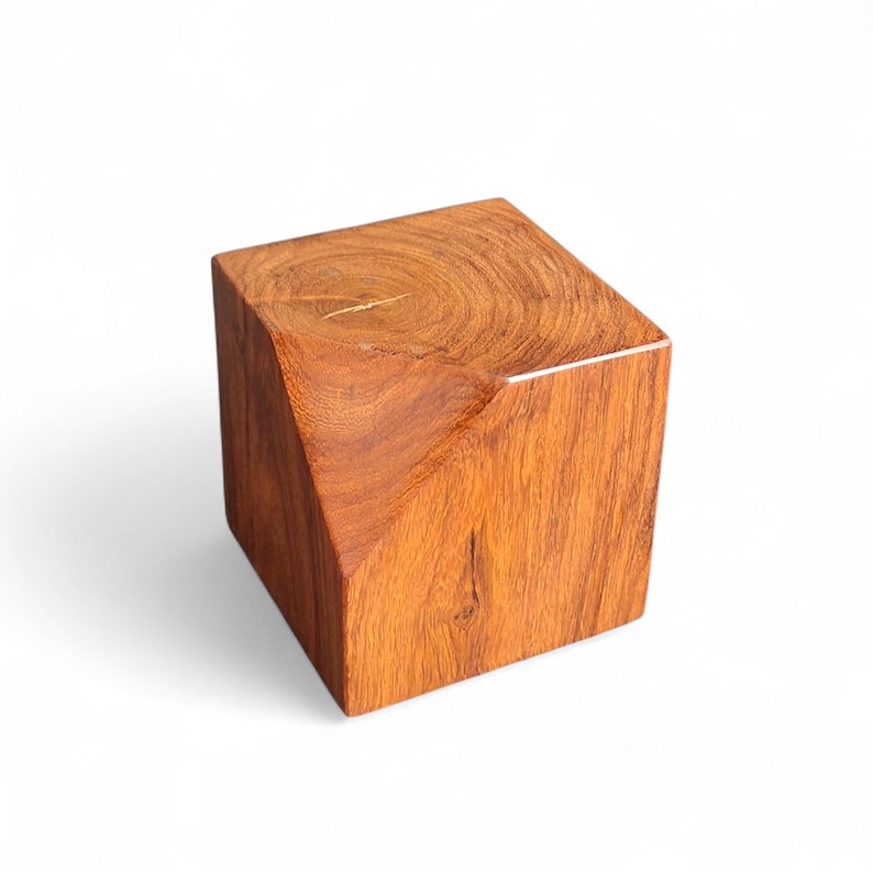 May include: A solid, geometric wooden cube with a diagonal cut on one side. The cube is made of reddish-brown wood, showcasing the natural grain and texture. The design is modern and minimalist, suitable for decorative purposes.