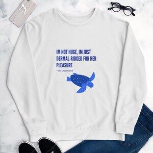 May include: White sweatshirt with the text "IM NOT HUGE, IM JUST DERMAL-RIDGED FOR HER PLEASURE" and a blue turtle graphic. The text is in blue, and the turtle is a darker blue with white dots. The sweatshirt is a casual style.