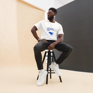 May include: White t-shirt with blue text and a blue whale graphic. The text reads "IN HOT WATER, OR JUST DERMAL ADAGES FOR HER PLEASURE". The shirt is worn with black jeans and white sneakers.