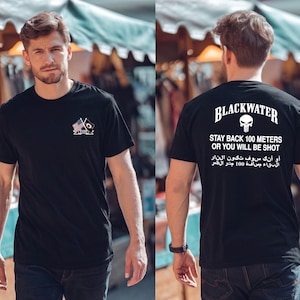 Puede incluir: Camiseta negra con un pequeño emblema en la parte delantera y el texto "BLACKWATER" con un gráfico de calavera en la parte trasera. La parte trasera de la camiseta también tiene el texto "STAY BACK 100 METERS OR YOU WILL BE SHOT" y texto en otro idioma.