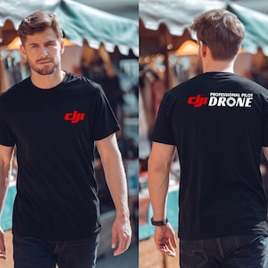 May include: Black crew neck t-shirt with a red logo on the front and the words "PROFESSIONAL PILOT DRONE" on the back. The t-shirt is worn by a person in an outdoor setting.