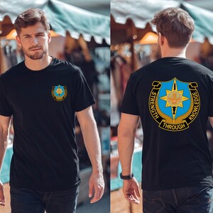 May include: Black t-shirt with a crest design on the front and back. The front crest is a blue and gold emblem. The back of the shirt features a larger crest with the words "STRENGTH THROUGH KNOWLEDGE".