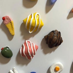 Puede incluir: Colección de imanes en miniatura con forma de alimentos coloridos. Incluye un cono de helado amarillo con una bola rosa y una cereza roja, un cuadrado amarillo con glaseado blanco y un pastel rosa con glaseado blanco.