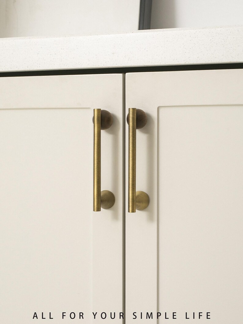 May include: Close-up of two cream-colored cabinet doors with vertical brass-colored handles. The handles are cylindrical with rounded ends. The text "ALL FOR YOUR SIMPLE LIFE" is at the bottom of the image.