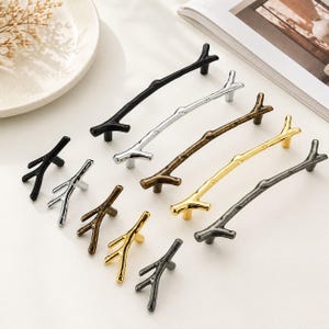 May include: A collection of decorative cabinet pulls and knobs in various metallic finishes, including black, silver, bronze, and gold. The hardware is designed in the shape of tree branches, offering a natural and rustic aesthetic. Ideal for kitchen or furniture upgrades.
