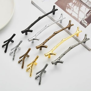 May include: A collection of decorative cabinet pulls and knobs in various metallic finishes. The hardware is designed to resemble tree branches, with options in black, silver, bronze, gold, and pewter. These decorative pulls and knobs are ideal for adding a natural touch to furniture.