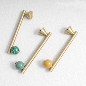 May include: Three gold-toned cabinet pulls with a conical top and a straight handle. Each pull features a decorative, round, stone-like accent in green, green and black, and yellow.