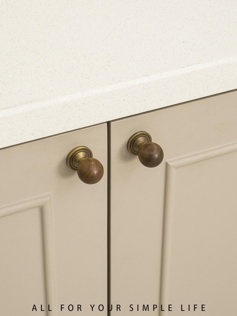 May include: Close-up of two cabinet doors with round, wooden knobs and brass hardware. The doors are a neutral beige color, and the countertop above is white. The text "ALL FOR YOUR SIMPLE LIFE" is at the bottom.
