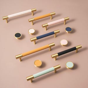 May include: A selection of cabinet handles and knobs in various colours. The bar handles have gold-coloured ends and coloured central sections in white, orange, pink, navy, yellow, and black. The knobs have matching colours.