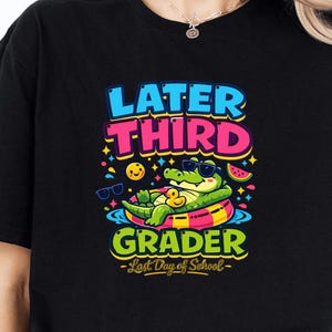 Könnte beinhalten: Schwarzes T-Shirt mit einem farbenfrohen Aufdruck. Das Design zeigt den Text "LATER THIRD GRADER" mit einem Cartoon-Alligator mit Sonnenbrille auf einem Schwimmring. Enthält den Text "-Last Day of School-".