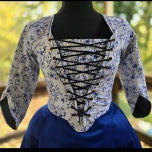 May include: A white and blue floral print corset top with black lacing. The sleeves are three-quarter length, and the bottom portion is a deep blue. The corset is displayed on a black mannequin.