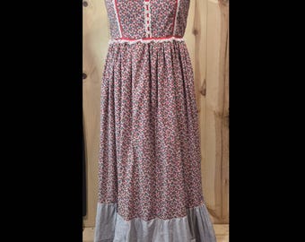 May include: A vintage floral print maxi dress on a mannequin. The dress features a red and white floral pattern on a dark background, with red trim and white lace detailing. The skirt has a tiered design with blue floral accents.