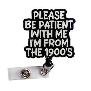 May include: A black and white badge reel with the text "PLEASE BE PATIENT WITH ME I'M FROM THE 1900'S". The badge has a white plastic clip and a black retractable cord with a metal clasp.