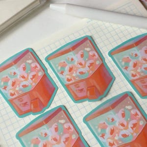 May include: A collection of stickers featuring a gumball machine design. The stickers have a red and orange body with a teal outline. The gumball machine is filled with colorful gumballs in shades of pink, orange, and blue.