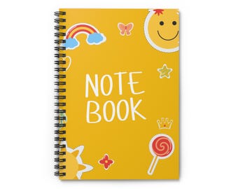 Op de afbeelding: Een spiraalgebonden notitieboek met een felgele kaft. De kaft toont de witte woorden "NOTE BOOK", samen met kleurrijke illustraties van een regenboog, een smiley, sterren, een vlinder, een bloem, een kroon en een lolly.