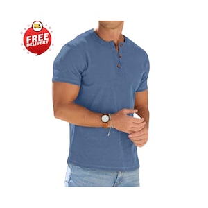 May include: A short-sleeved, blue Henley shirt with three brown buttons. The shirt is made of a textured fabric and is paired with blue jeans. A watch with a brown leather strap is visible on the wrist.